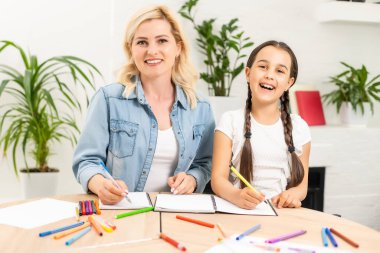 Anne ve kız güzel ve mutlu anneler günü için kağıt ve kalemlerle birlikte masaya oturarak bir kart yapın.