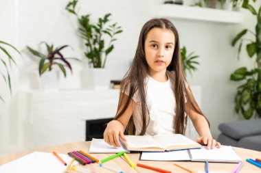 Onun yakın plan portresi oldukça çekici küçük, neşeli, uzun saçlı kız masa başında oturuyor ve açık beyaz sınıf odasında makale ödevi yazıyor..