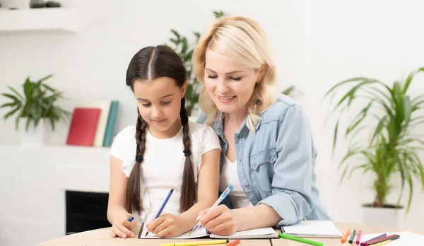 Mother and small 8s daughter at home have fun painting together with colors. Happy mom or nanny and little girl child enjoy drawing. — Stock Photo, Image