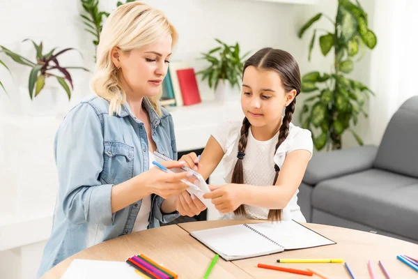 Moeder en dochter mooi en gelukkig maken een kaart voor moeders dag zitten samen aan tafel met papier en potloden — Stockfoto