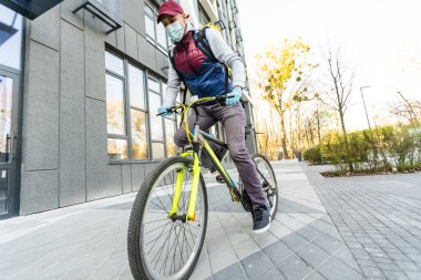 Genç kurye, şehirde bisiklet süren sarı bir termal sırt çantasıyla yiyecek getiriyor. Yemek servisi konsepti