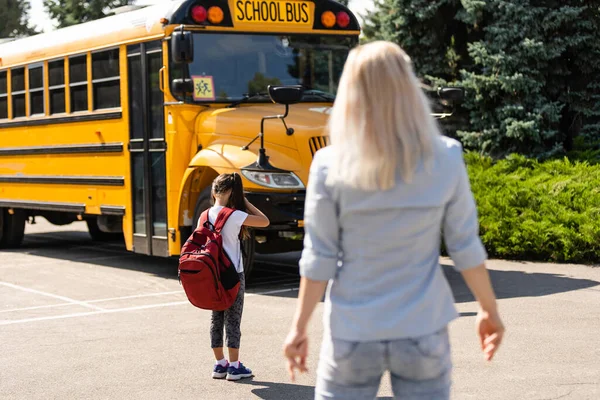 Mamá lleva a su hija a la escuela cerca del autobús escolar. de vuelta a la escuela — Foto de Stock