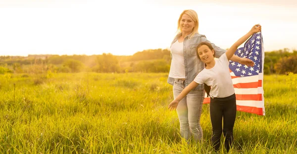 Madre e hija con bandera americana en un hermoso campo — Foto de Stock