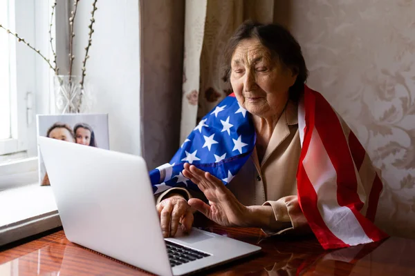 Independence Day celebration after quarantine. Granny looking at laptop screen and celebrating national holiday with her family online, care about senior people, personal technology, focus on woman