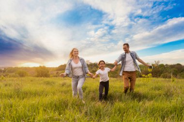 Park akşam ışığında mutlu bir aile. Güneşin ışıkları. Anne, baba ve bebek gün batımında mutlu yürüyüşler. Mutlu aile kavramı.