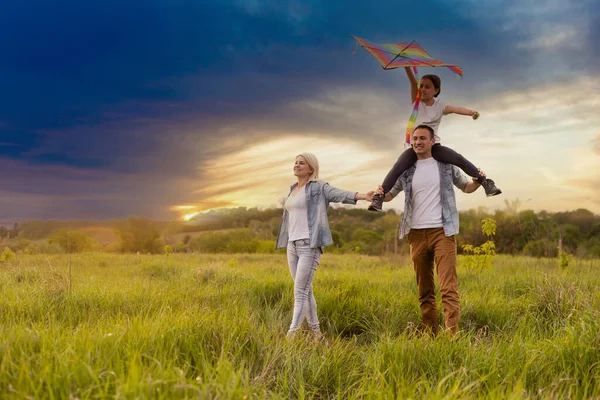 Feliz familia padre, madre e hija lanzan una cometa en la naturaleza al atardecer — Foto de Stock