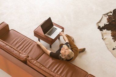 Uzaktan kumandalı ev işi, karantina sırasında serbest çalışma. Gülümseyen bayan rahat oturma odasında dizüstü bilgisayarda oturuyor ve çalışıyor.