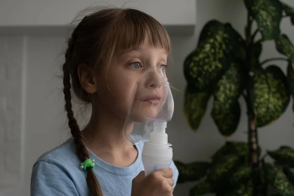 La niña hace inhalación con un nebulizador. niño enfermo sosteniendo el inhalador en la mano y respira a través de un inhalador en casa — Foto de Stock