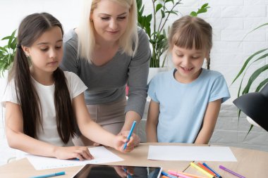 Anne ve iki kız evde ödev yapıyor ve kitap okuyor.