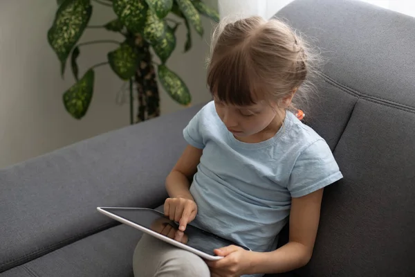Menina inteligente usando computador tablet enquanto sentado no sofá na sala de estar em casa — Fotografia de Stock