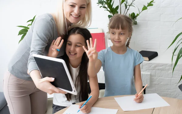 여교사나 양어머니가 귀여운 초등 학교 여학생 이 책상에 앉아 숙제하는 것을 도와 주고 있습니다. 어머니와 자녀 가집에서 공부하면서 공책에서 쓰는 법을 배우는 모습 — 스톡 사진