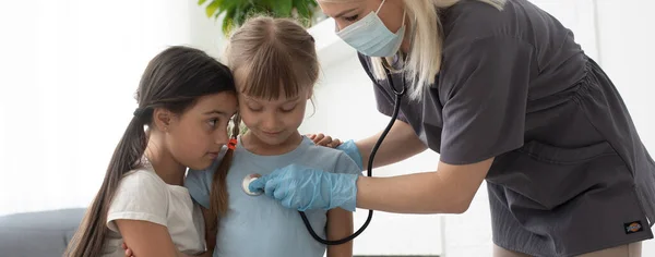 Médecin avec un stéthoscope vérifie deux petites filles — Photo