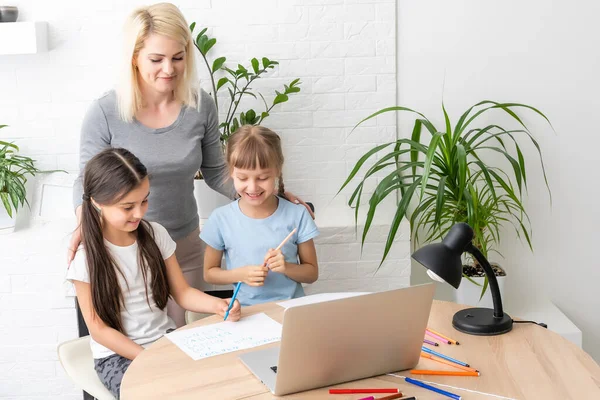 인터넷을 배우는 어린 두 딸들은 어머니의 도움 과 가르침, 격려를 받아 컴퓨터를 사용하여 숙제를 한다. 딸 과 여동생은 함께 집에서 교육을 받는 것을 기뻐하고 있다 — 스톡 사진
