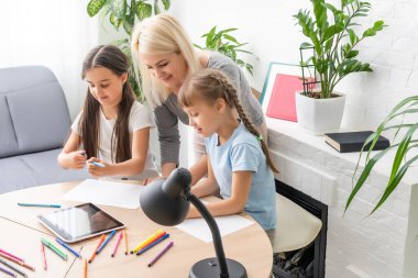 Anne ve iki kız evde ödev yapıyor ve kitap okuyor.