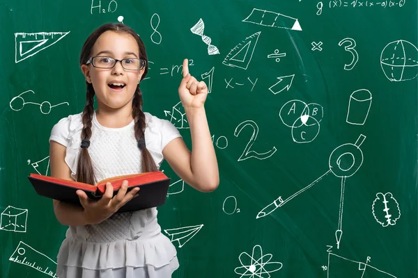 Linda menina de pé e segurando livro sobre fundo branco — Fotografia de Stock