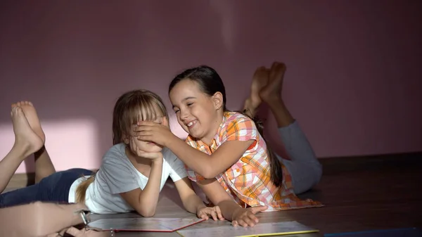 Aile, eğlence ve çocukluk konsepti. Mutlu kız kardeşler yerde yatar ve evde ödev yaparlar. — Stok fotoğraf