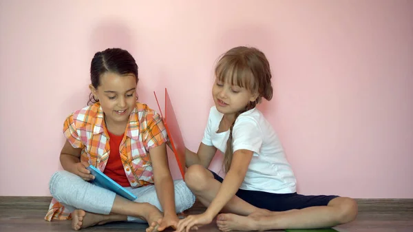 A kislányok könyvet olvasnak a nappaliban. Okos iskolás lányok csinálják a házi feladatukat suli után. Oktatás és távoktatás gyerekeknek. Magántanuló a karantén alatt. Maradj otthon szórakozni.. — Stock Fotó