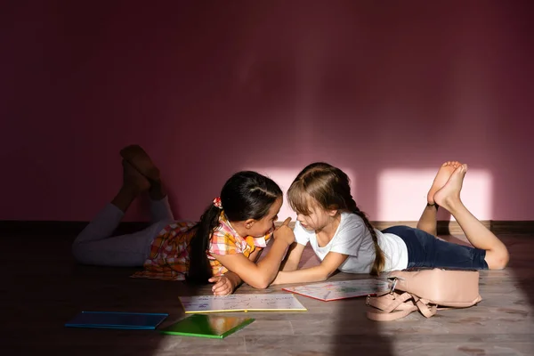 Raparigas a ler um livro na sala de estar. Estudantes inteligentes a fazerem os trabalhos de casa depois da escola. Educação e educação à distância para crianças. Ensino em casa durante a quarentena. Fique em casa entretenimento. — Fotografia de Stock