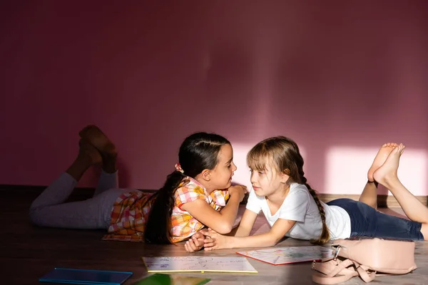 Concepto de familia, ocio e infancia - hermanas felices tumbadas en el suelo y haciendo los deberes en casa — Foto de Stock