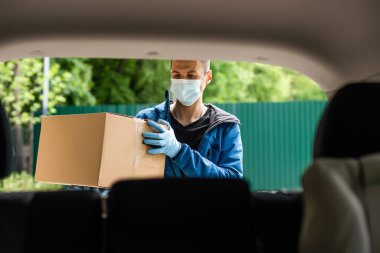 Arabanın yanındaki adam. Teslimat üniformalı bir adam. Tıbbi maskeli bir adam. Coronavirus konsepti.