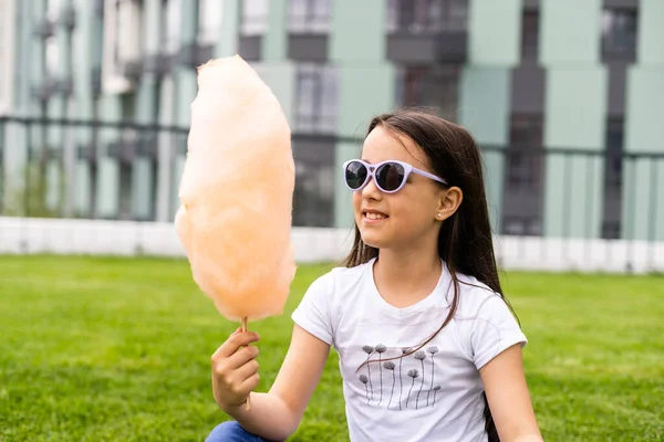 Adorable y bonita niña comiendo dulces de algodón. Niño feliz, niño comiendo hilo de caramelo con emociones en el parque en verano o primavera. — Foto de Stock