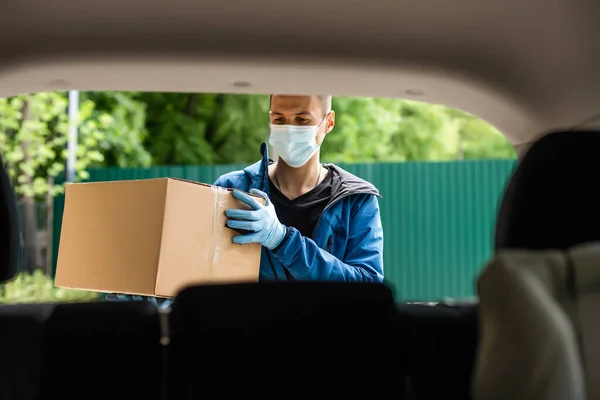 Man by the car. Guy in a delivery uniform. Man in a medical mask. Coronavirus concept.