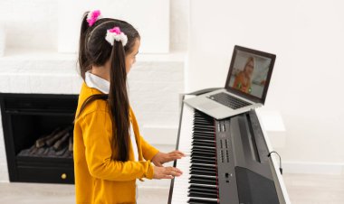 Evde eğitim gören küçük bir kız, okul öğretmeninin internet müziğine bağlı bilgisayardan piyano öğreniyor. Yeni normal yaşam tarzı ve eğitim, ev konseptinde öğrenim.