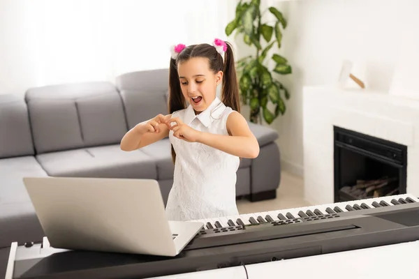 Homeschool pequena menina criança aprendendo piano a partir de computador conectando-se à música da internet aula on-line pelo professor da escola. Novo estilo de vida normal e educação, estudo do estudante em casa conceito. — Fotografia de Stock