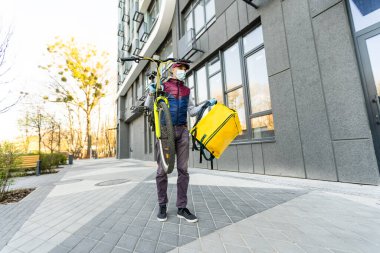 Genç kurye, şehirde bisiklet süren sarı bir termal sırt çantasıyla yiyecek getiriyor. Yemek servisi konsepti