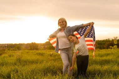 Güzel bir tarlada Amerikan Bayrağı taşıyan anne ve kızı.
