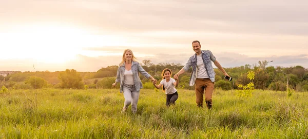 Familia feliz en la luz de la tarde del parque. Las luces de un sol. Mamá, papá y bebé caminan felices al atardecer. El concepto de una familia feliz — Foto de Stock