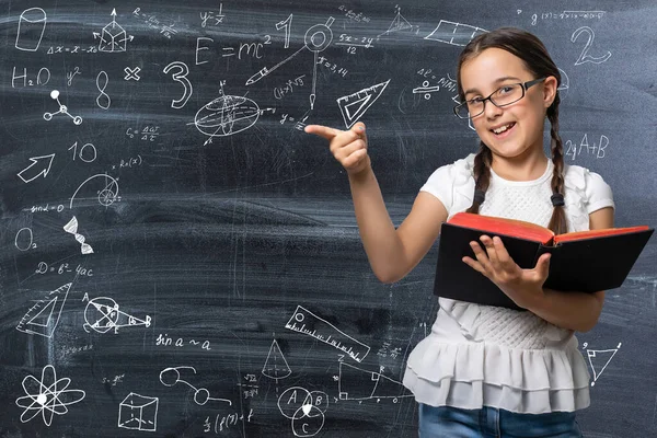 Linda menina de pé e segurando livro sobre fundo branco — Fotografia de Stock