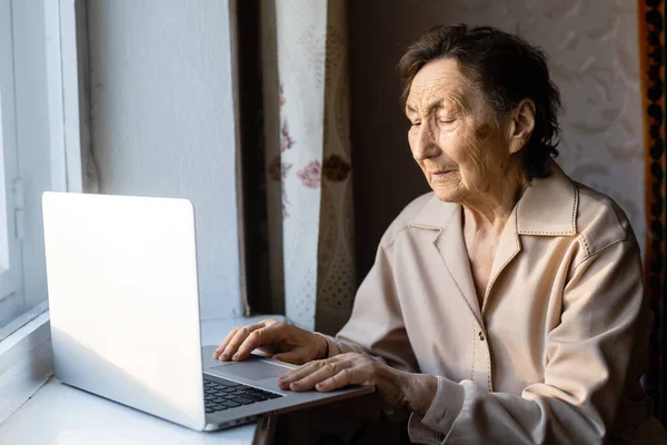 Senior woman use laptop. She looks very surprised. Surfing in a browser and social media. Laptop on the table. Using technology in old age concept — Stock Photo, Image