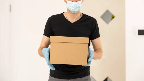 Närbild händer leverans man håller paket för att leverera. Kurir hand hålla brun låda isolerad på grå bakgrund. Detalj av leverans man bär kartong paket med etikett med kopia utrymme. — Stockfoto