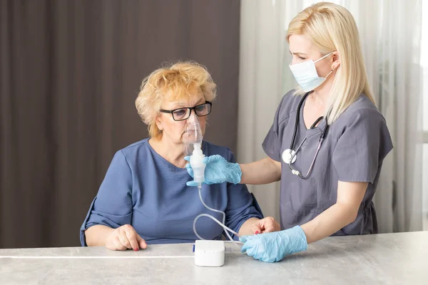 Доктор в медицинской маске делает вдох пожилой женщине. Борьба с перегрузкой носа и ринитом. — стоковое фото