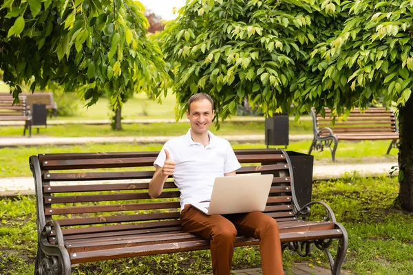 年轻人坐在公园的长椅上，膝上型电脑 — 图库照片
