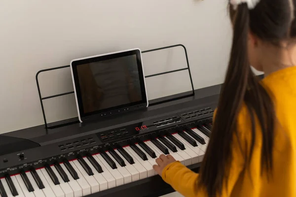 귀엽고 진지 한 어린 소녀가 흰색으로 전기 피아노를 연주하고 있다 — 스톡 사진