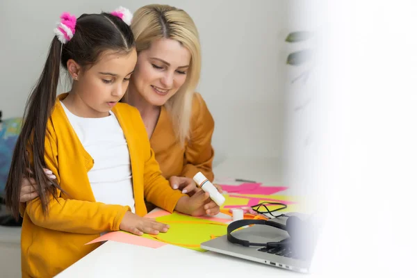 Bella giovane madre che aiuta la figlia più giovane con i compiti. — Foto Stock