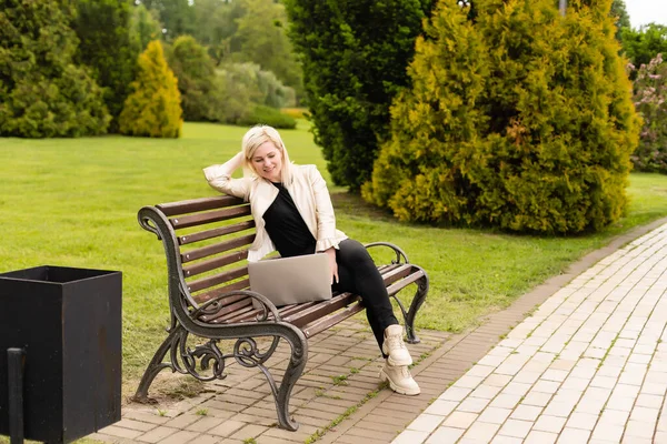 Jeune femme d'affaires attrayante utilisant un ordinateur portable PC tout en étant assis sur un banc en bois dans un parc de la ville. — Photo
