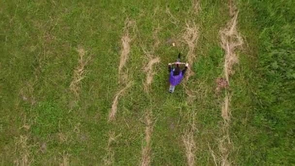 Aerial drone top view flight above girl rides bicycle across the field — Stock video