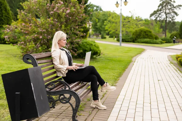 Jovem mulher de negócios atraente usando um computador portátil pc enquanto sentado em um banco de madeira em um parque da cidade. — Fotografia de Stock