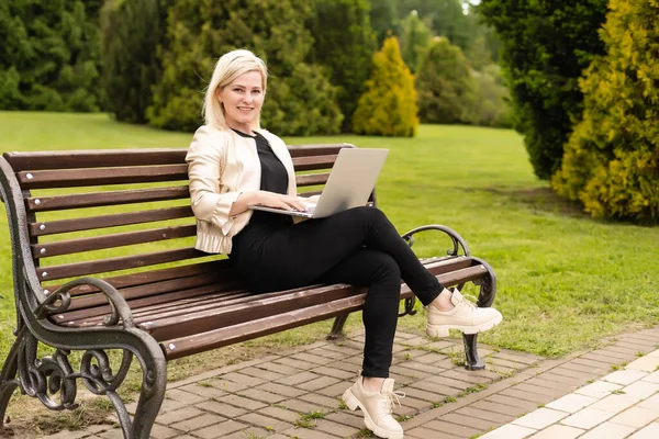 Молода приваблива бізнес-леді, використовуючи комп'ютер ноутбука ПК, сидячи на дерев'яній лавці в міському парку . — стокове фото