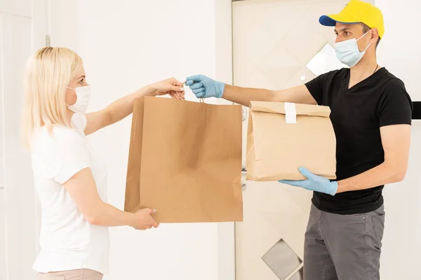 Koerier in beschermend masker en medische handschoenen levert afhaalvoedsel. Leveringsdienst onder quarantaine, ziekte-uitbraak, coronavirus covid-19 pandemie. — Stockfoto