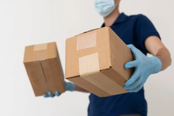 Man from delivery service in t-shirt, in protective mask and gloves giving food order and holding boxes over white background.