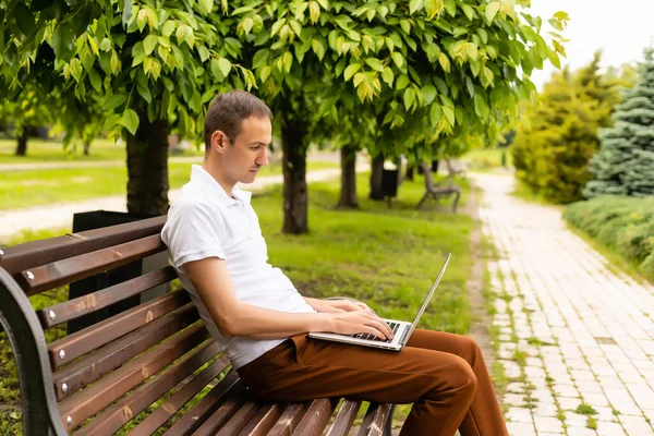 Jeune homme assis sur le banc du parc avec ordinateur portable sur ses genoux — Photo