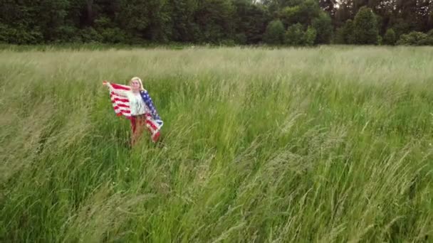 Американка с гордостью держит американский флаг на закатном поле, празднует 4 июля — стоковое видео