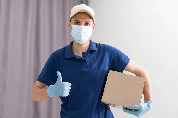 Man from delivery service in t-shirt, in protective mask and gloves giving food order and keping box over white background. — Φωτογραφία Αρχείου