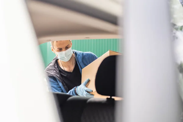 Курьер почтовой доставки, одетый в защитную маску перед грузовым фургоном, доставляет коробку с коронавирусной болезнью или COVID-19 — стоковое фото