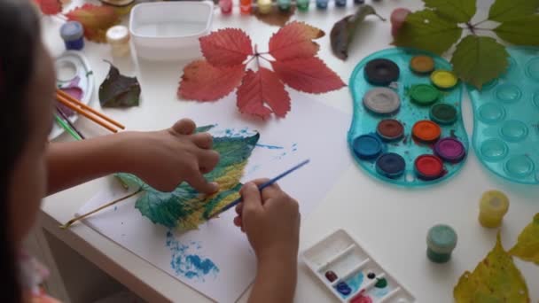 Kleines Mädchen malt auf herbstgelben Blättern mit Gouache, Kinderkunst, Kinder Kreativität, Herbstkunst. — Stockvideo