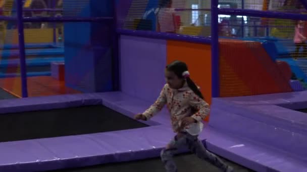 Little kid girl has fun playfully jumping and rolling in trampoline amusement park playground — Αρχείο Βίντεο